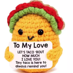 Hand-crocheted Taco doll holding a white positive affirmation sign, sitting on a wooden table.