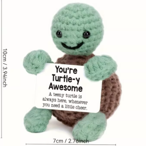 Hand-crocheted Turtle doll holding a white positive affirmation sign, sitting on a wooden table.