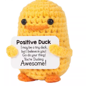 Hand-crocheted Duck doll holding a white positive affirmation sign, sitting on a wooden table.