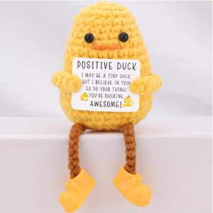 Hand-crocheted Duck doll holding a white positive affirmation sign, sitting on a wooden table.